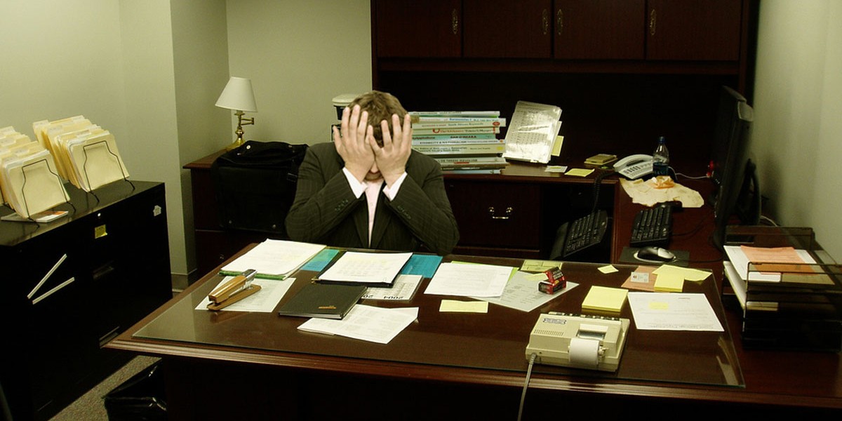 Frustrated man at a desk (Image by LaurMG [CC BY SA 3.0], via Wikimedia Commons)