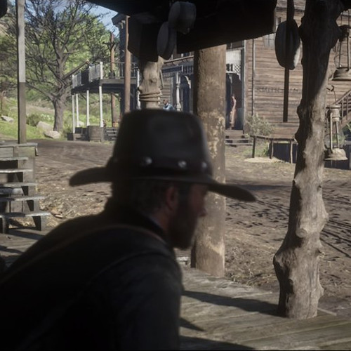 Eine Person sitzt in Red Dead Redemption 2 auf einer Bank in Valentine und schaut dem Treiben auf der Straße zu.