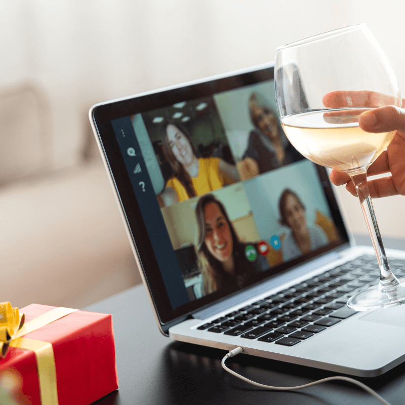 Jemand sitzt mit Wein beim Videochatten und hat ein Geschenk daneben liegen