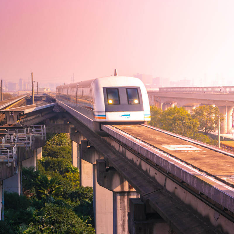 Eine Magnetschwebebahn fährt im Licht der Morgensonne über eine auf Stützen stehende Fahrstrecke.