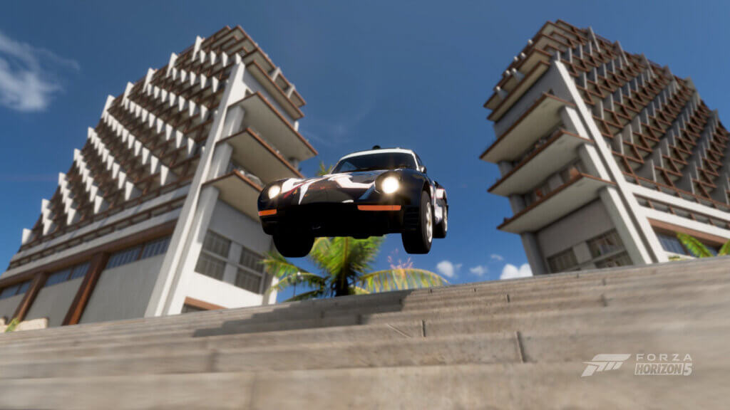 Ein alter Porsche springt durch zwei große Hotelgebäude eine große Treppe runter.