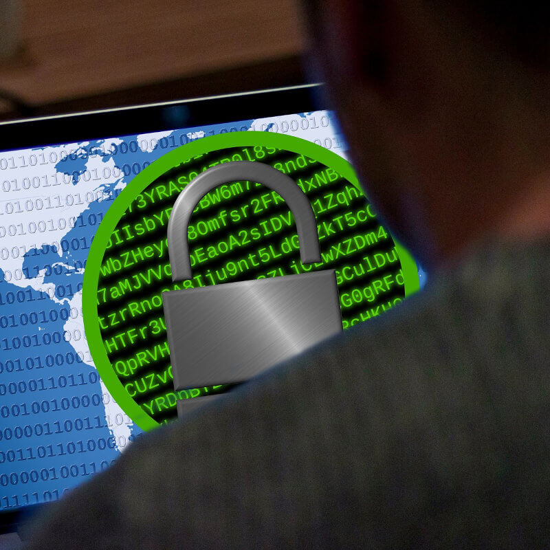 Mann sitzt vor einem PC. Der Bildschirm ist mit einsen und nullen beschrieben in der Mitte eine Art Meldung und ein Schloss, dass für Cybersicherheit steht.