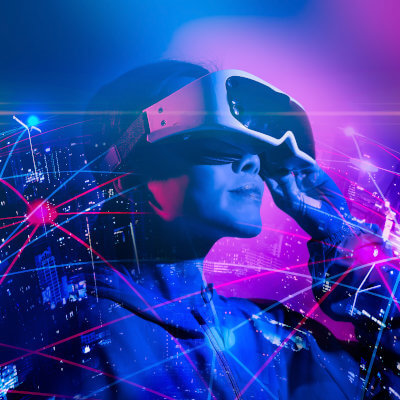Eine Frau trägt eine Virtual Reality Brille. Um sie herum zeichnet sich eine vvernetzte Welt ab.