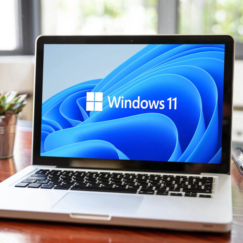 Laptop auf einem Tisch. Auf dem Bildschirm ist das Windows 11-Logo zu erkennen.