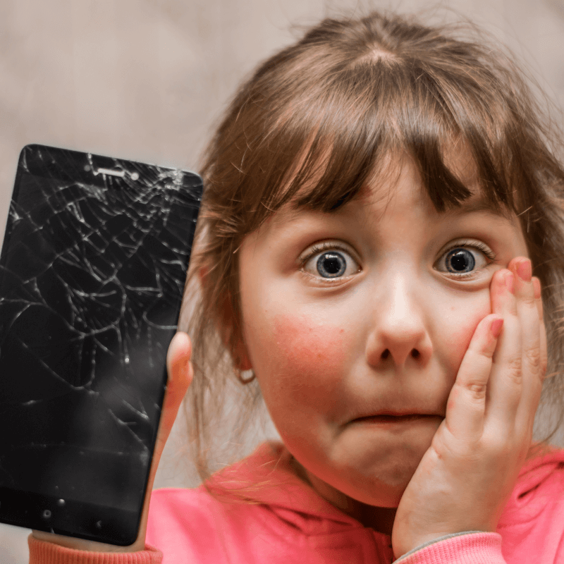 Ein erschrocken-trauriges Mädchen mit einem kaputten Smartphone in der Hand.