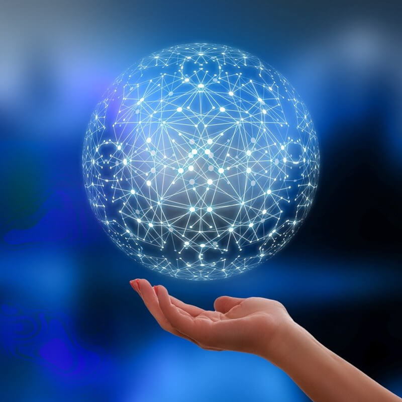Eine geöffnete Hand über der eine virtuell wirkende Kugel aus durch Lichtstrahlen verbundenen Knotenpunkten schwebt.