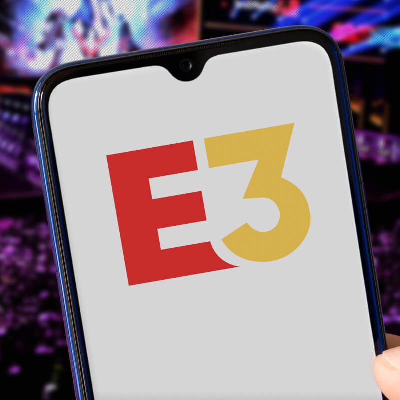 E3-Logo auf einem Smartphone. Im Hintergrund Publikum einer Veranstaltung.