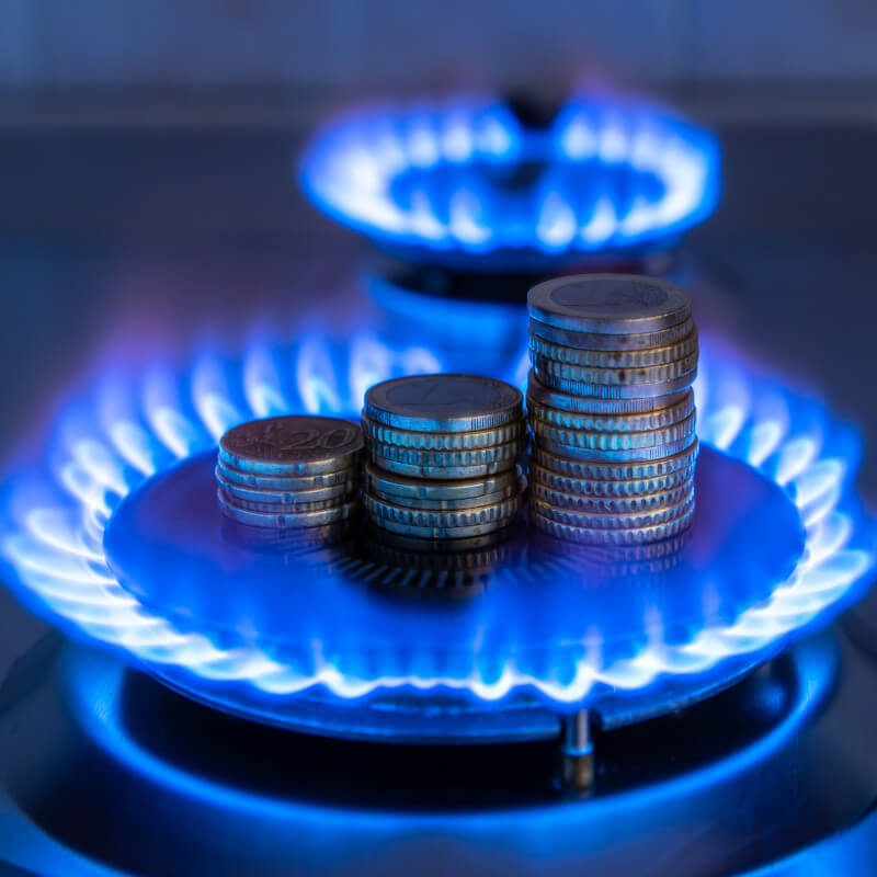 Eine gasbetriebene und gerade brennende Herdplatte, in dessen mitte drei Stapel mit Euromünzen stehen.