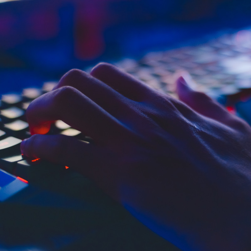 Eine Hand auf einer von innen rot beleuchteten Tastatur in einem sonst nicht beleuchtetem Raum.