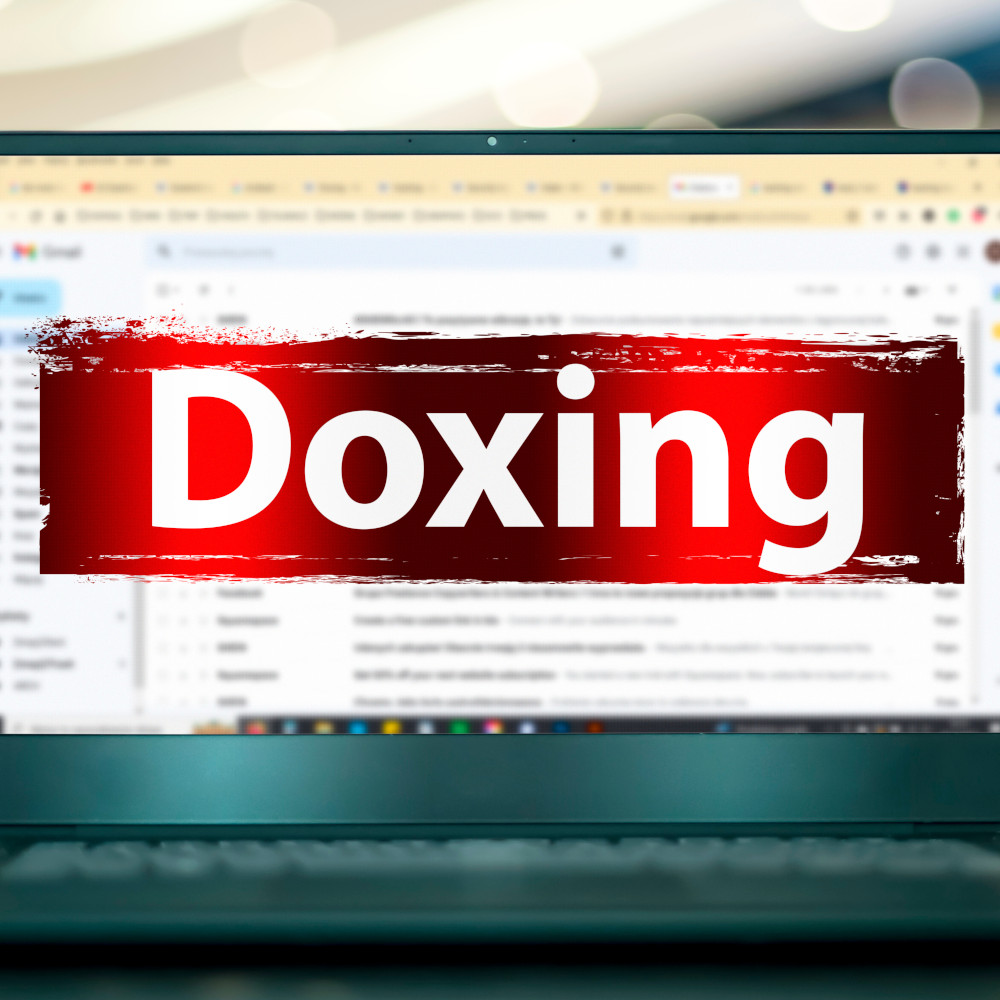 Ein aufgeklappter Laptop mit geöffnetem E-Mail-Programm. Davor ist das Wort "Doxing" mit warnend rotem Hintergrund.