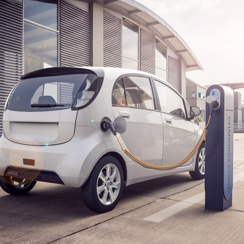 ein weißes Elektroauto wird bei Sonnenschein an einer Ladesäule aufgeladen.