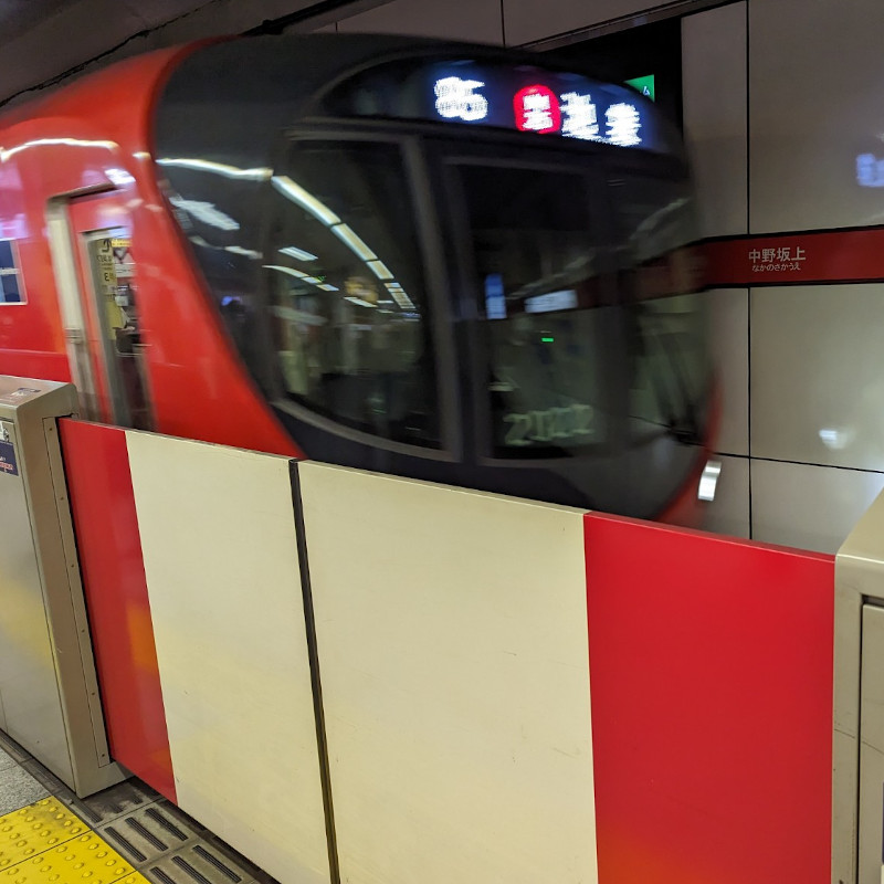 eine rote U-Bahn fährt in einen Bahnsteig ein. DIe Zugänge sind mit Barrieren abgesichert.