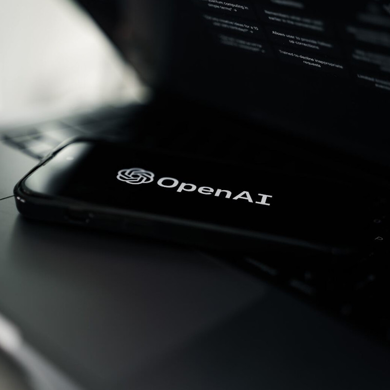 Ein Smartphone auf einem Laptop. Auf dem Smartphone-Bildschirm ist das Logo von Open AI zu sehen.