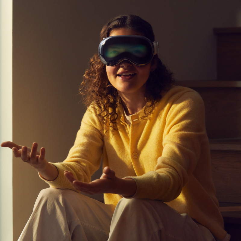 Eine junge Frau sitzt auf einer Treppenstufe und trägt eine Apple Vision Pro. Ihre Augen sind über das Front-Display zu erkennen.
