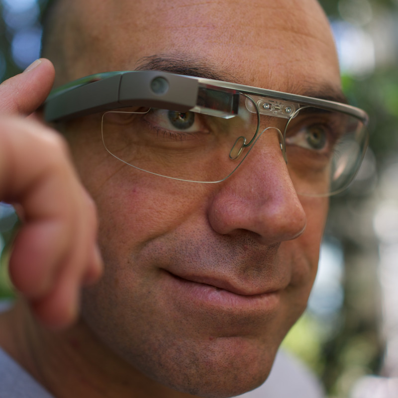 Ein Mann trägt eine Google Glass-Brille und bedient sie mit einem Finger am Rahmen.