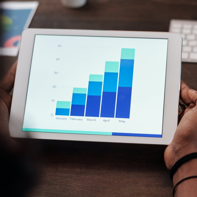 Eine Person hält ein Tablet in der Hand, auf dem ein nicht weiter spezifiziertes Säulendiagramm für die Monate Januar bis Mai zu sehen ist.