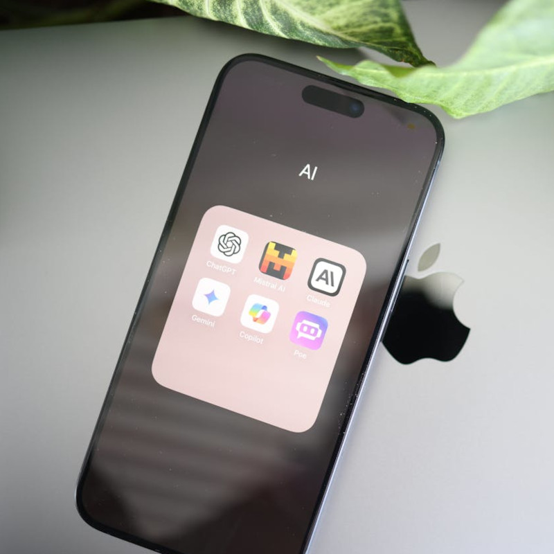 Smartphone mit mehreren KI-Apps auf der Nutzeroberfläche liegt auf einem Macbook.