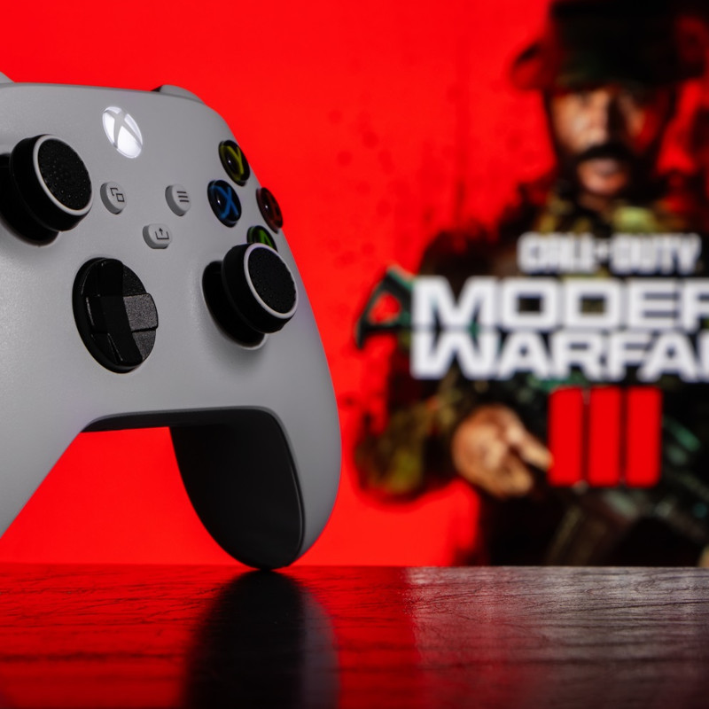 Ein Xbox Series Controller auf dem Tisch, im Hintergrund sieht man etwas verschwommen das Logo von Call of Duty: Modern Warfare 3.