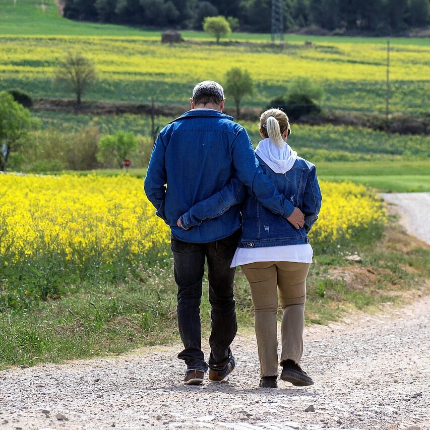 Paar läuft Arm in Arm über Feldweg mit Blumen im Hintergrund
