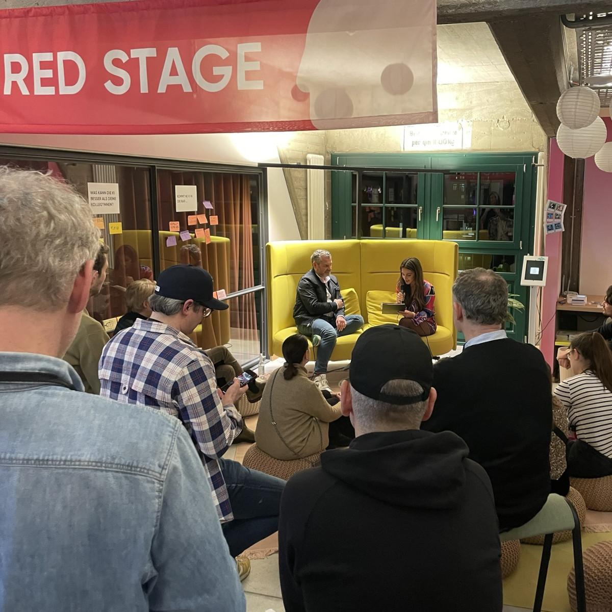 Mehrere Besucher sitzen um eine Bühne im SPACE Hamburg. Zwei Personen sind dort auf einem gemütlichen Sofa im Talk.