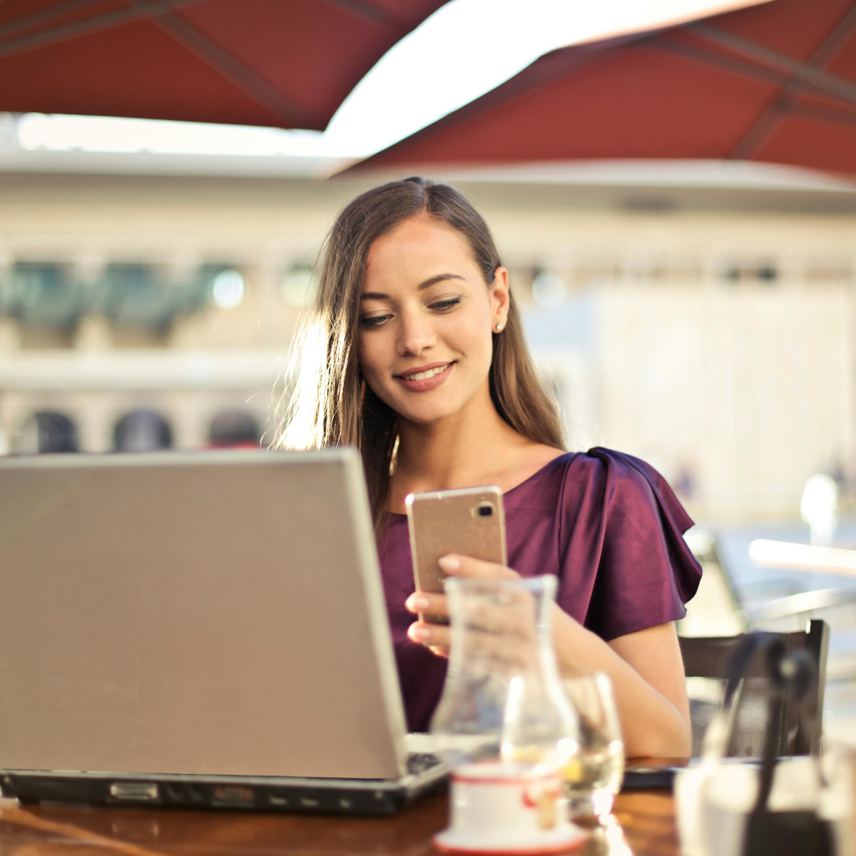 Eine junge Frau sitzt im Café und nutzt zeitgleich Laptop und Smartphone.