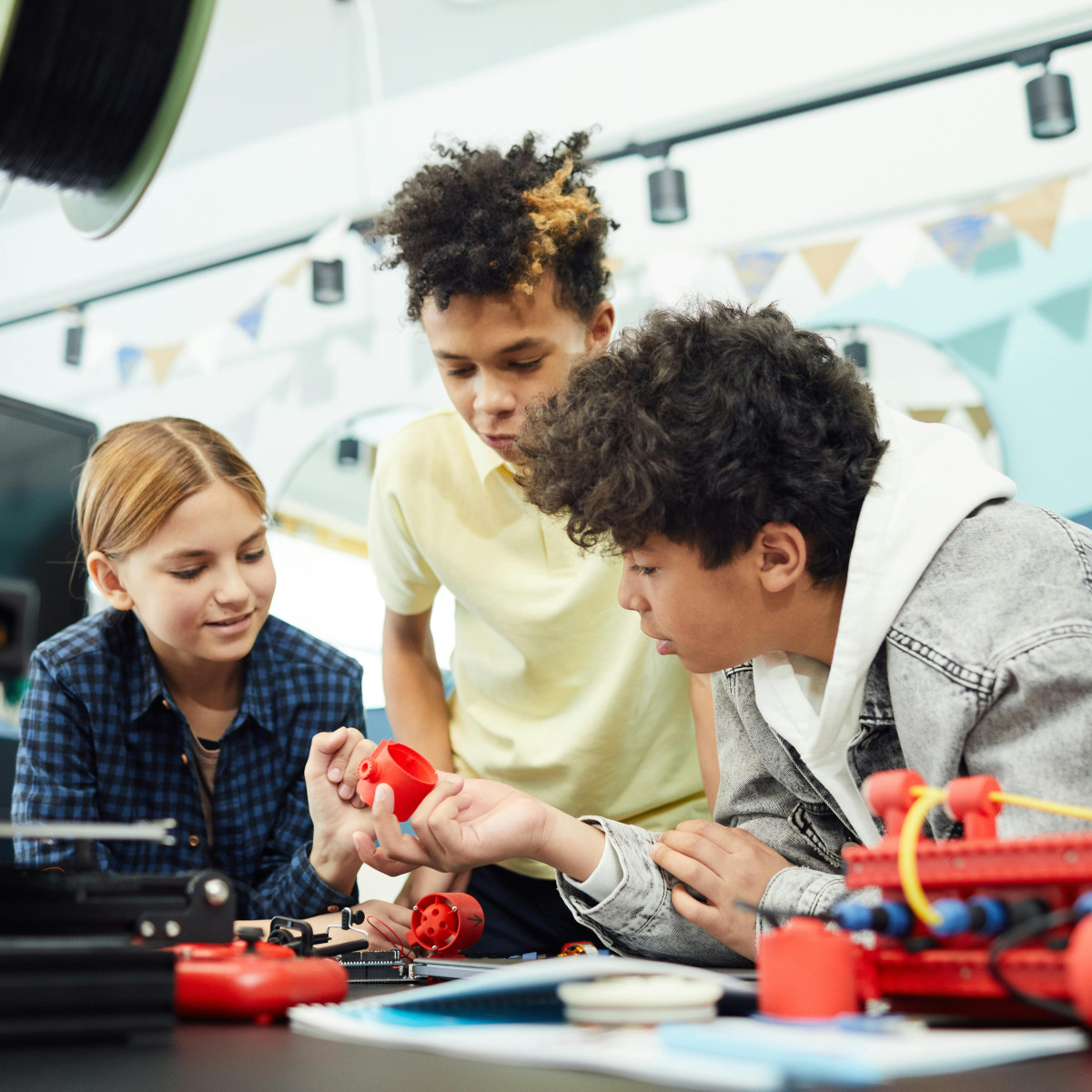 Drei Kinder beugen sich über einen Tisch und interagieren miteinander in einer Gruppenarbeit. Auf dem Tisch sind Robotikmaterialien.