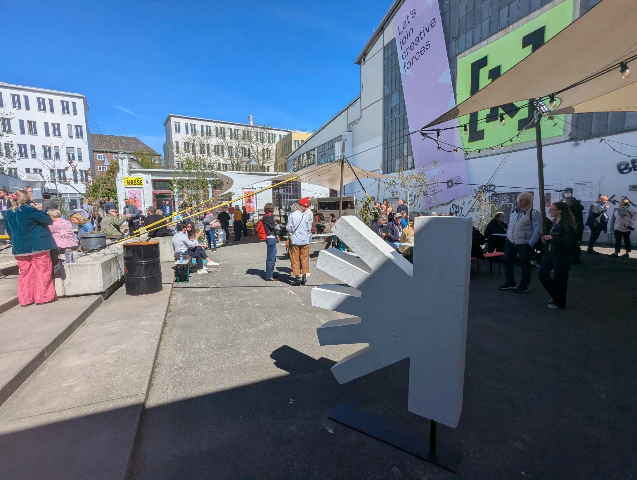 Blick in den Außenbereich von Kampnagel mit vielen Besucher*innen und einem Aufstelllogo von Kreativ Hamburg