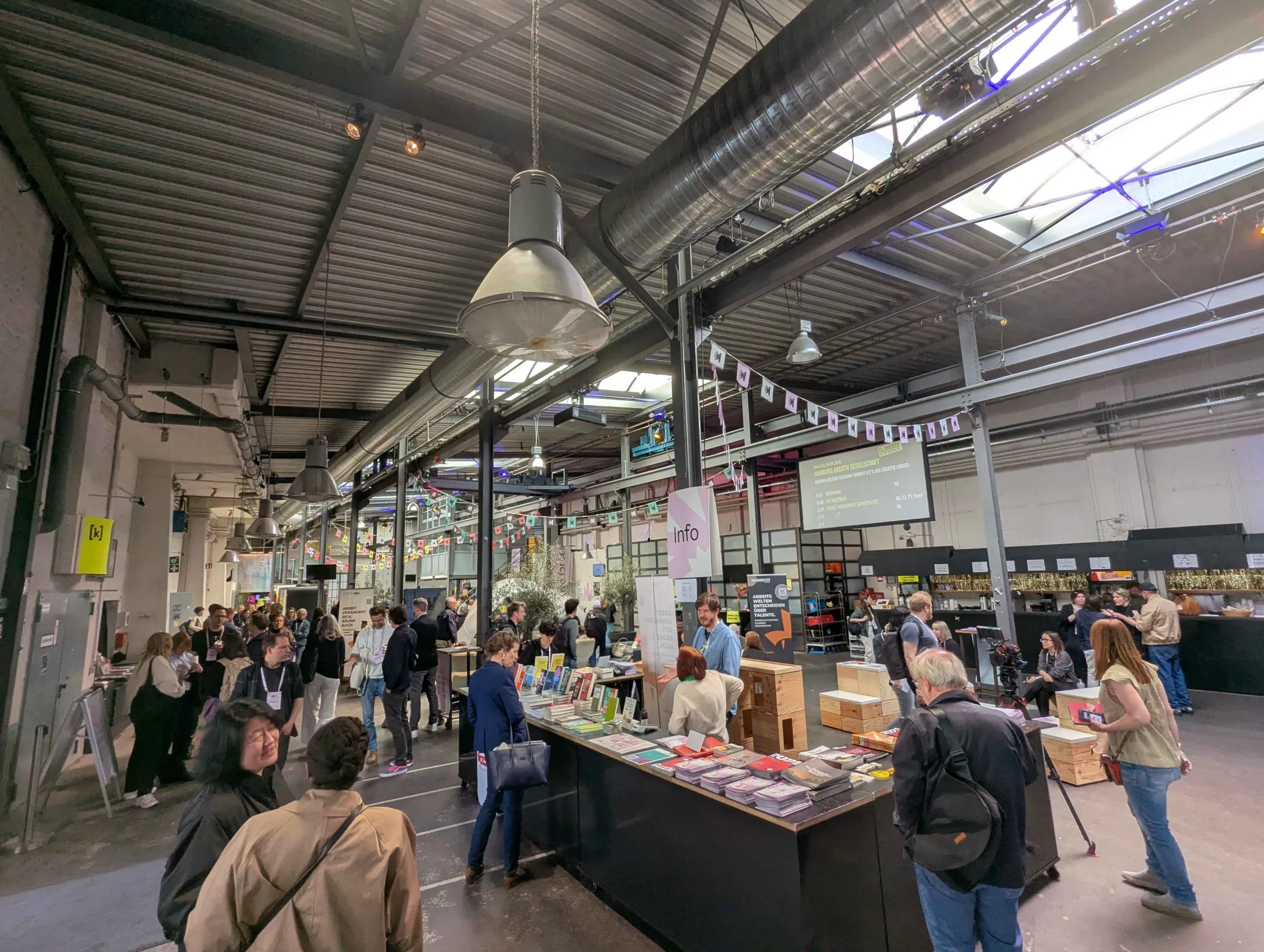 Das Kampnagel-Foyer voller Menschen, in der Mitte des Bildes ist ein Stand mit diversen Büchern und Broschüren