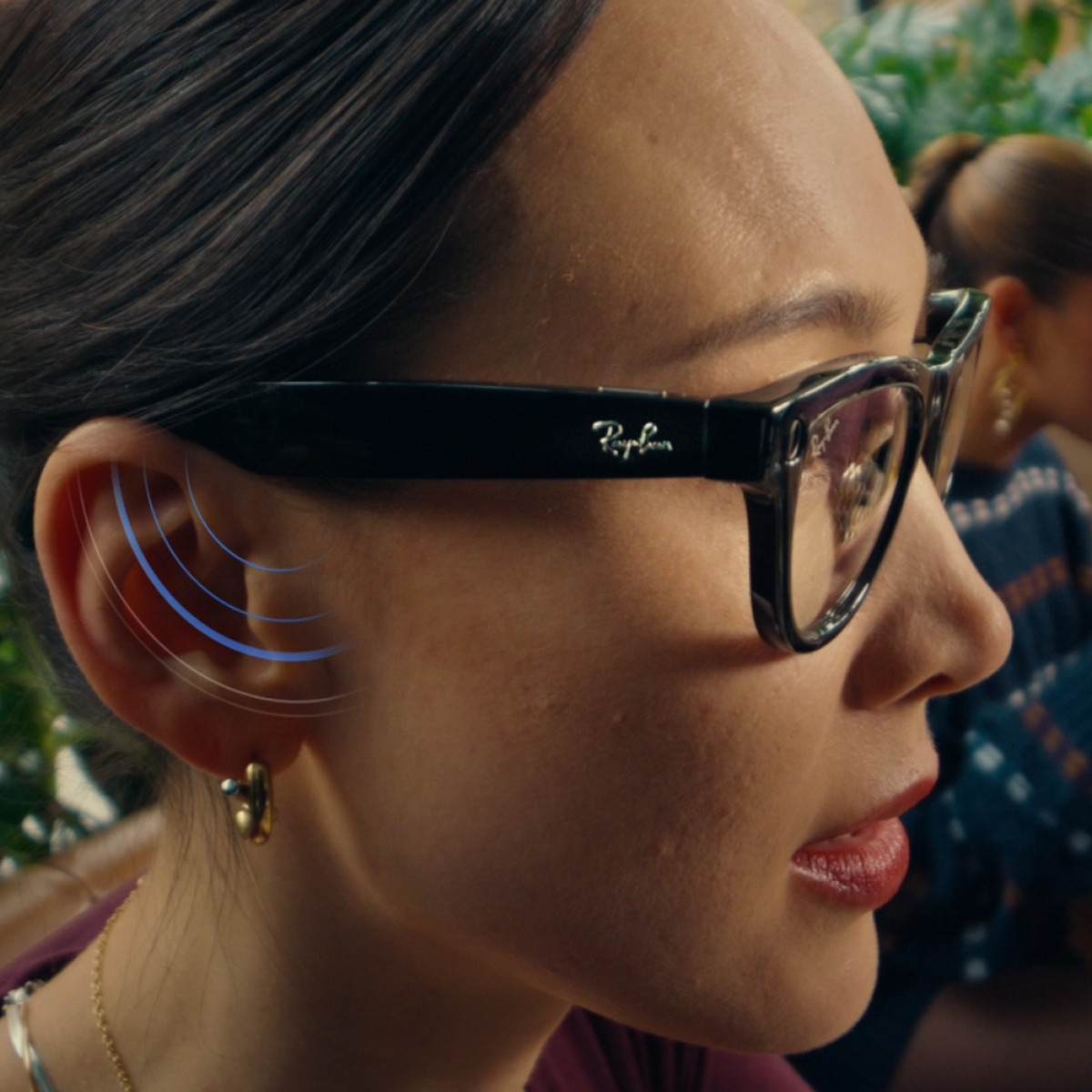 Frau trägt die Meta x RayBan Brille, an ihrem Ohr werden durch blaue Signalstreifen der Lautsprechereffekt der Brille signalisiert
