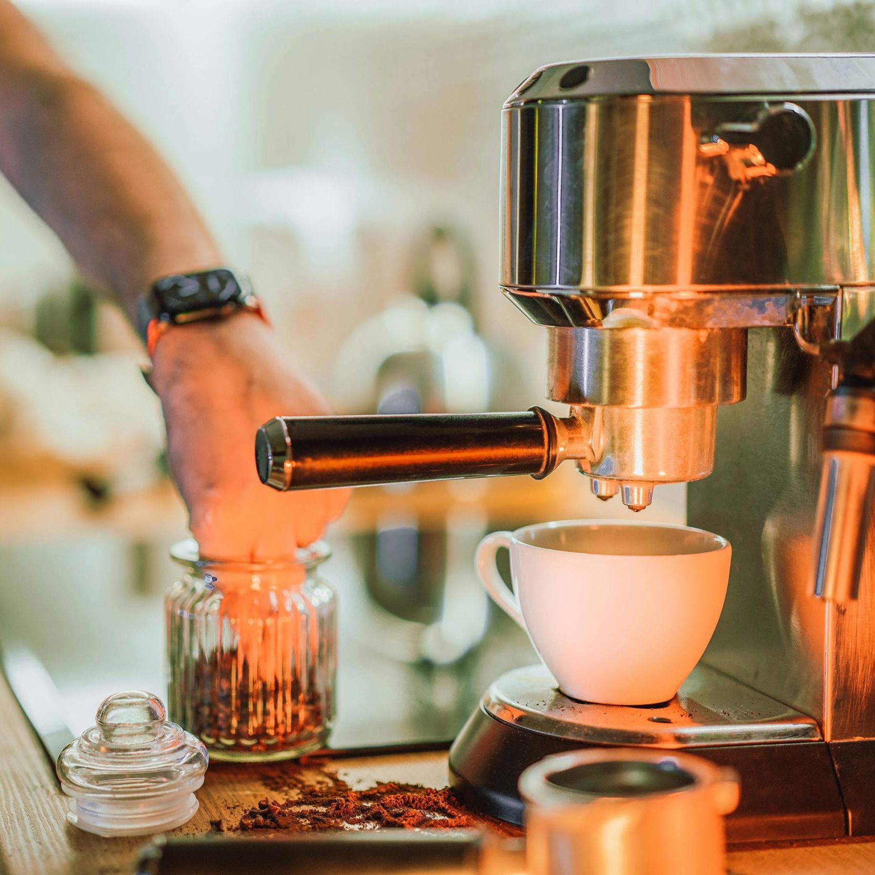 Hand bedient einen Siebträger an einer Edelstahl-Espressomaschine, davor eine weiße Tasse