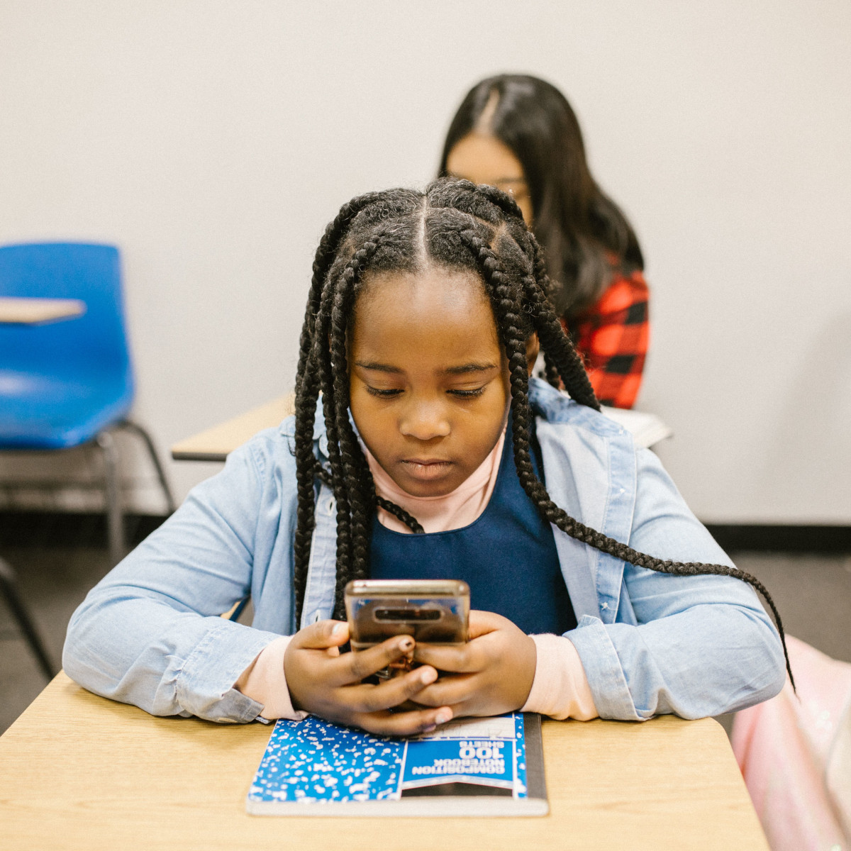Ein junges Mädchen sitzt an einem Tisch in ihrem Klassenzimmer und schaut auf ihr Smartphone.